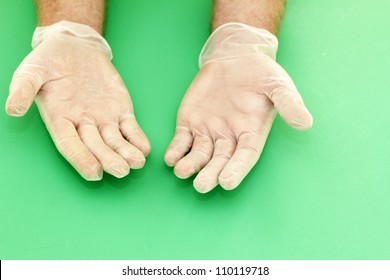 Human Hands Wearing Powdered Vinyl Gloves With Palms Up On A Green Background.