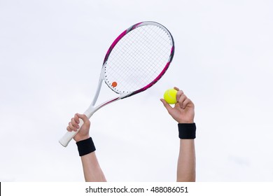 Human hands with wristbands holding tennis ball and a racket on background of the sky