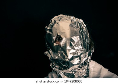 Human Head Is Wrapped With Aluminium Foil. Only The Right Eye Is Looking Throug A Hole In The Foil, Black Background