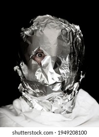 Human Head Is Wrapped With Aluminium Foil. Only The Right Eye Is Looking Throug A Hole In The Foil, Black Background