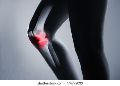 Human knee joint and leg in x-ray, on gray background. The knee joint is highlighted by red colour.