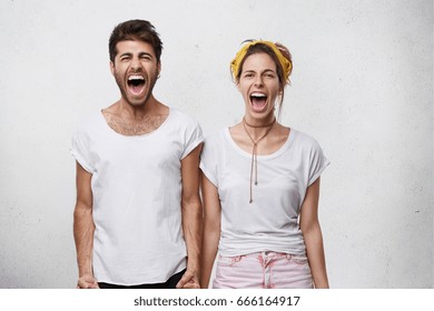 Human negative emotions, reaction, feelings and attitude. Waist-up portrait of stressed desperate young Caucasian couple screaming, shouting while quarreling indoors, standing close to each other