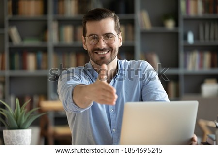 Human resource agent male recruiter sit at desk extends his hand to camera for handshake greeting applicant showing polite gesture start job interview in modern office. Welcoming, cooperation concept
