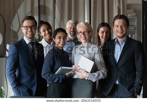 Human resource. Group portrait of smiling\
employees friendly team of diverse age race gender standing in\
office together. Successful motivated old young age multiethnic\
corporate staff look at\
camera