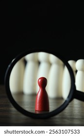 Human resources concept. Looking at red figure through magnifying glass on table against dark background, closeup