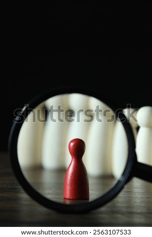 Human resources concept. Looking at red figure through magnifying glass on table against dark background, closeup