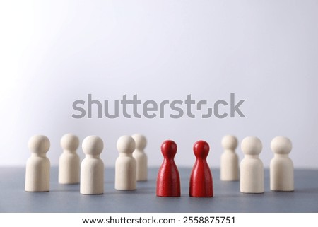 Human resources concept. Red figures among wooden ones on table against light background, closeup. Space for text