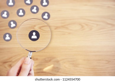 Human resources management and recruitment concept, Hand holding magnifying glass search people paper icon on top desk.