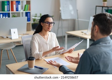 Human resources manager communicating with vacancy applicant during employment interview at modern office. HR professional speaking to job candidate, holding CV indoors