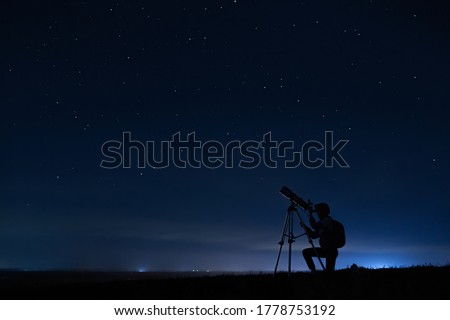 Human silhouette and telescope, a woman looks through a telescope at the starry sky. Night sky, stars, long exposure, astronomy