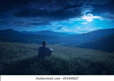 Human sitting on a hill and enjoy full moon rising in a starry sky above the night mountain valley. - Powered by Shutterstock