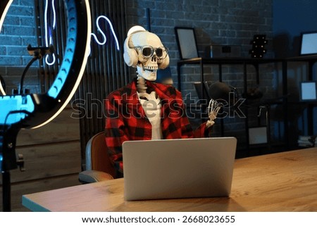 Human skeleton model with laptop at table in dark podcaster's studio