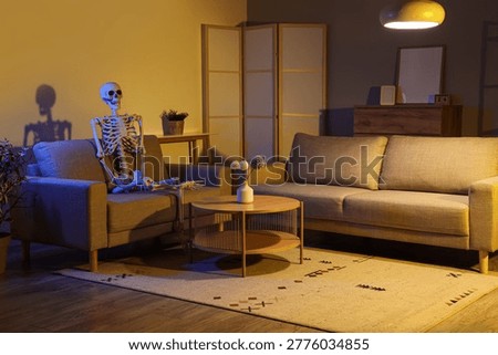 Human skeleton model sitting on grey couch in dark living room