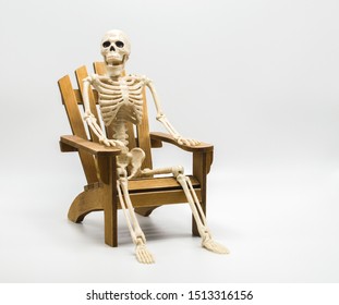 Human Skeleton Sitting In A Wooden Adirondack Chair Isolated On White