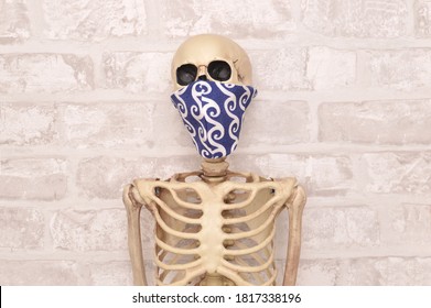 Human Skeleton Wearing Face Mask In Front Of White Brick Wall