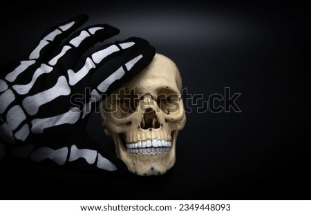 Human skull on a dark background with a skeleton hand. Dark and gloomy skull. Background for Halloween. Decorative skull model.

