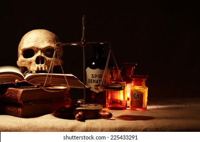 Human skull on old books near weight scales and ancient glass flasks
