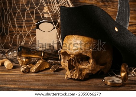 Human skull with pirate hat, golden nuggets, bottle of rum and travel equipment on brown wooden background