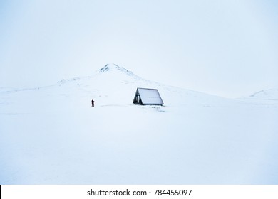 Human stand in front of snow white mountain peak and cute shack in white nature 