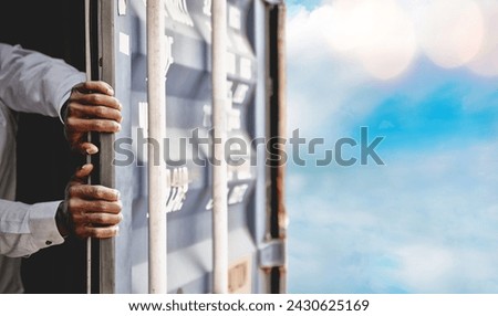 Human trafficking concept : Hands of a stateless black man in a container with the door opened to escape his confinement wanting freedom to the beautiful outside world.