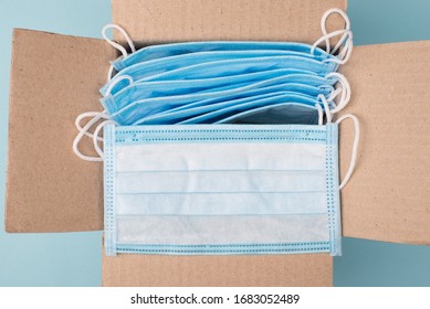 Humanitarian Aid Help Concept. Top Above Overhead Close Up View Photo Of Open Unpacked Unwrapped Paper Box With Lot Of Medical Masks On Blue Background