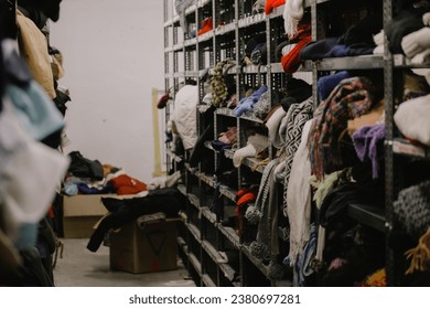 Humanitarian aid station, interior of industrial warehouse with used clothes for poor, refugees, vulnerable people. Shelves, rows of clothes second hand. Stock clothing section collection disordered. - Powered by Shutterstock