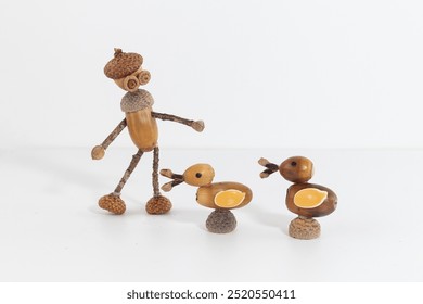 Humanoid acorn figurine and two acorn ducks in a creative nature scene. Woodland art with acorn bodies, twig limbs, and detailed features. Ideal for rustic crafts and seasonal themes.
