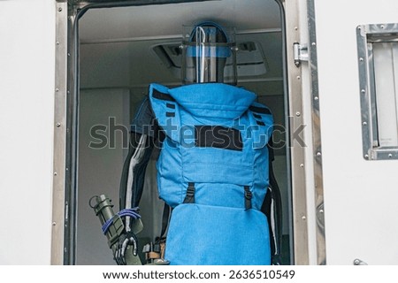 Humanoid robot in EOD suit within vehicle interior, artificial diffused lighting, blue-gray armor with insignia, possibly control room, science fiction realism blend