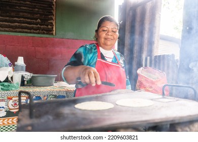 Humble Woman From Nicaragua Preparing Tortillas On A Metal Griddle. Latin American People In Their Daily Lives