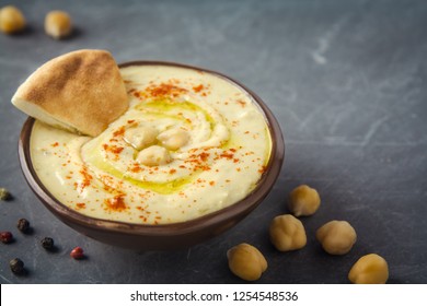 Hummus in a bowl and pita bread on grey background. Mediterranean snack, vegetarian healthy food concept. Top view, flat lay, copy space.