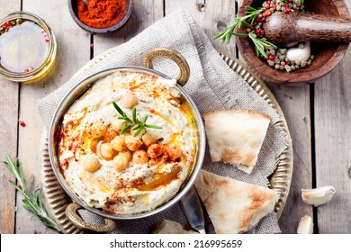 Hummus, chickpea dip, with rosemary, smoked paprika and olive oil in a metal authentic bowl with pita on a wooden background. 