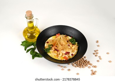 Hummus Fatteh Dish Prepared From Cooked Chickpeas, Roasted Bread Dices, Special Sauce Of Olive Oil, Nuts, Ghee, Pomegranate Grains And Spices Beside An Olive Oil Bottle.