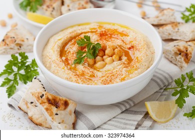 Hummus or houmous, appetizer made of mashed chickpeas with tahini, lemon, garlic, olive oil, parsley and paprika on wooden table