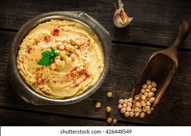 Hummus in metal bowl on dark wooden table. Selective focus.