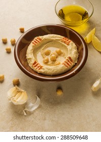 Hummus- Middle  eastern dip or spread made with chickpeas, garlic, lime, olive oil and tahina. Raw ingredients spread around the traditional hummous bowl.  - Shutterstock ID 288509648