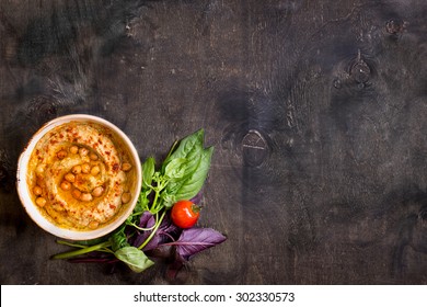 Hummus on a plate with cherry tomatoes and herbs on a dark wooden background. Middle eastern dish. Space for text