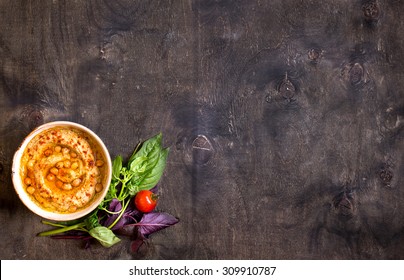 Hummus on a plate with cherry tomatoes and herbs on a dark wooden background. Middle eastern dish. Space for text