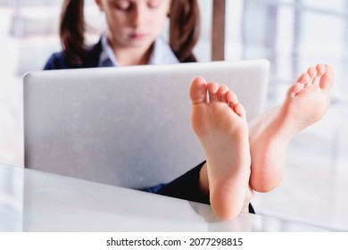 Humorales Bild von einem schönen jungen Geschäftsmädchen, das mit bloßen Füßen im Büro arbeitet. Selektiver Fokus auf die Füße.