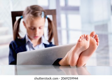 Nach dem Absturz arbeitet im Büro ein humorvolles Bild von Business-Child-Mädchen mit nackten Füßen auf dem Tisch. Selektiver Fokus auf bloße Füße