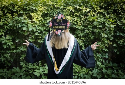 A Humorous Image Of A Woman In A Convocation Cap And Gown In Front Of A Green Leaf Hedge With Her Head Tilted Backwards To Show A Message On The Top Of Her Cap That Says 