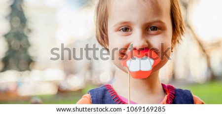 Humorous photo. Funny beautiful little child girl playing with fake lips and teeth.