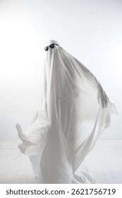Una foto humorística de una persona cubierta con una sábana blanca que actúa como un fantasma, con gafas de sol negras, aislada sobre un fondo blanco de estudio. Concepto minimalista y peculiar de Halloween o plantilla de meme divertido