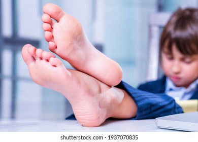 Humorous portrait of cute little business child girl with bare feet works remotely with laptop. Selective focus.