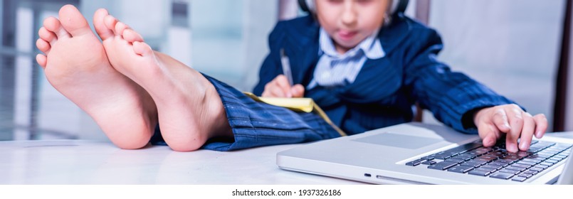 Humorous Portrait Of Cute Little Business Child Girl With Bare Feet Works Remotely With Laptop. Horizontal Image. Selective Focus On Bare Feet.