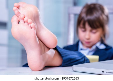 Humorous Portrait Of Cute Little Business Child Girl With Bare Feet Works With Laptop. Selective Focus On Bare Feet.