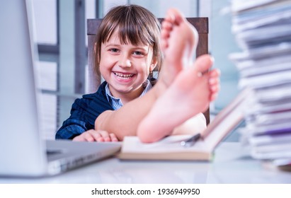 Humorales Portrait von sehr glücklichen kleinen Business-Kind Mädchen mit bloßen Füßen auf dem Tisch arbeitet mit Laptop und Dokumenten. Selektiver Fokus.