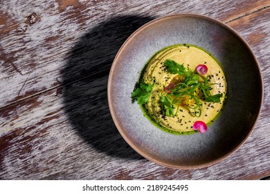 Humus with parsley, flower petals, chuka, sesame seeds, and sauce in a plate on a wooden table - Shutterstock ID 2189245495