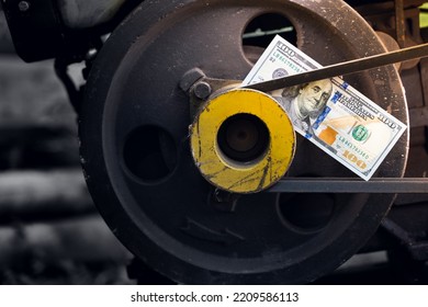 Hundred dollar bill close-up on an industrial background. Money on a belt driven tractor engine pulley. Production costs and the financial component of big business