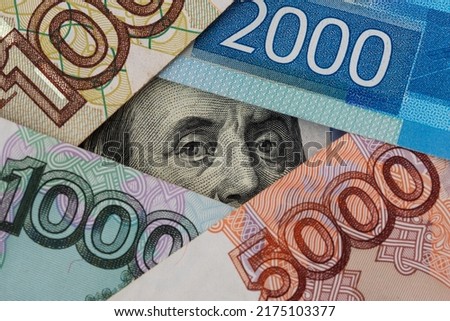 The hundred dollar bill with Franklin's portrait surrounded by russian banknotes of various denominations. Close-up of President Franklin's eyes. Concept of ruble exchange rate.
