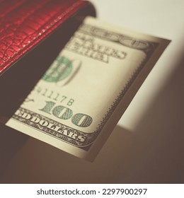 Hundred dollar bill sticking out of a red purse over sunny grey table with strong shadows. - Shutterstock ID 2297900297